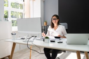 woman working in a nicely lit home office with huge monitor and a laptop